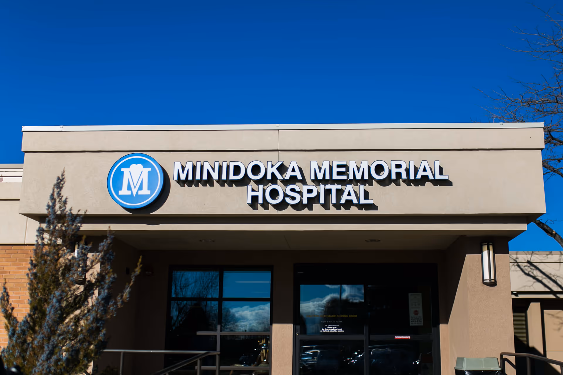 Exterior front view of Minidoka Memorial Hospital building under a clear blue sky, showing the hospital's name and logo above the entrance.