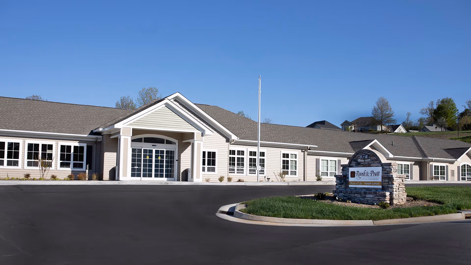 Exterior view of the Runk & Pratt Pearls of Life at Liberty Ridge senior living facility building under a clear blue sky, with a stone sign in front displaying the facility name.