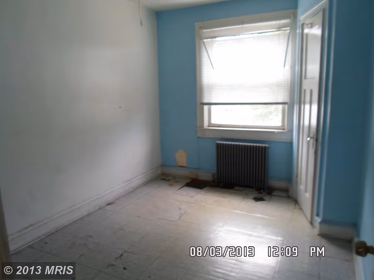 Empty small bedroom with blue walls, a window with blinds, a radiator under the window and a closet door.