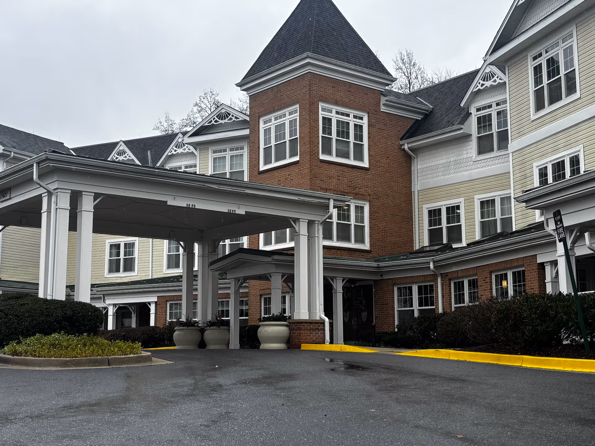 Front entrance with a covered porte-cochère of a multi-story senior living building with brick and light-colored siding.