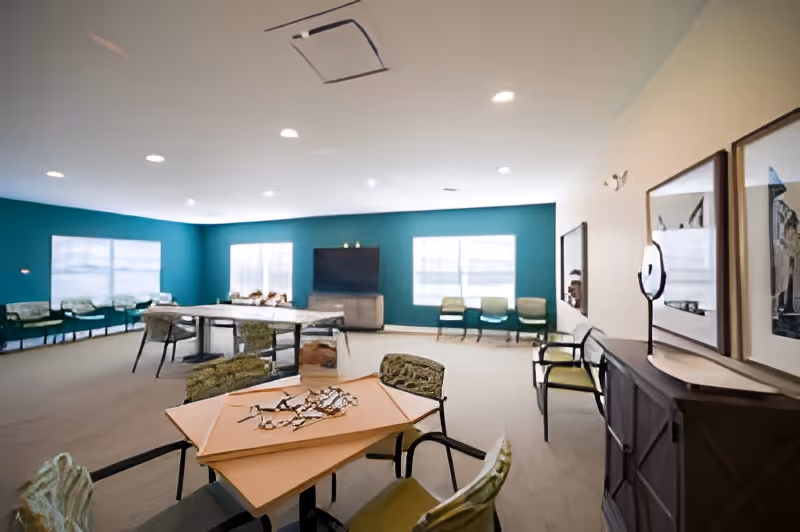Spacious senior communal room with tables and chairs, teal accent wall, windows, and a TV cabinet.