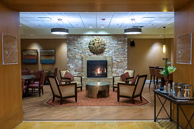 Cozy communal lounge with a stone fireplace, four armchairs arranged around a round coffee table and warm ambient lighting.