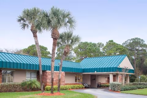 Exterior view of Huntington Place facility with teal roof, palm trees, and a driveway.