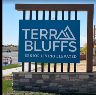 Outdoor sign for Terra Bluffs senior living facility with the tagline 'Senior Living Elevated', mounted on a stone base with a clear sky and road in the background.
