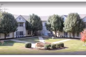 Two-story senior living building surrounding a landscaped courtyard with a central fountain, trees, and walkways.