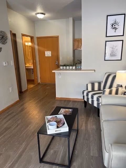 Living room area with a sofa, striped armchair, coffee table, and view into a hallway and kitchenette.