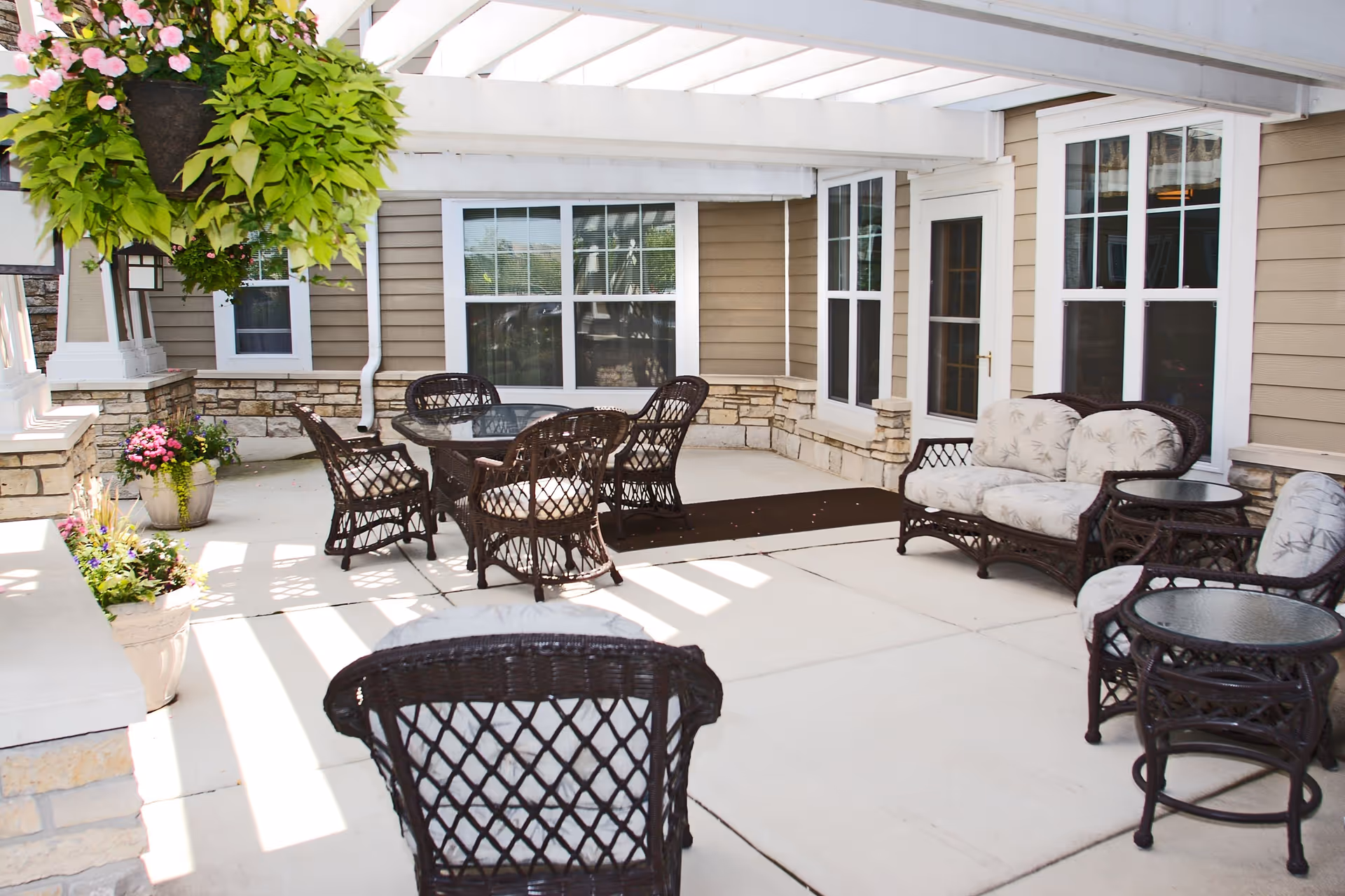 Covered outdoor patio with wicker chairs, a dining table, potted plants, and a pergola.