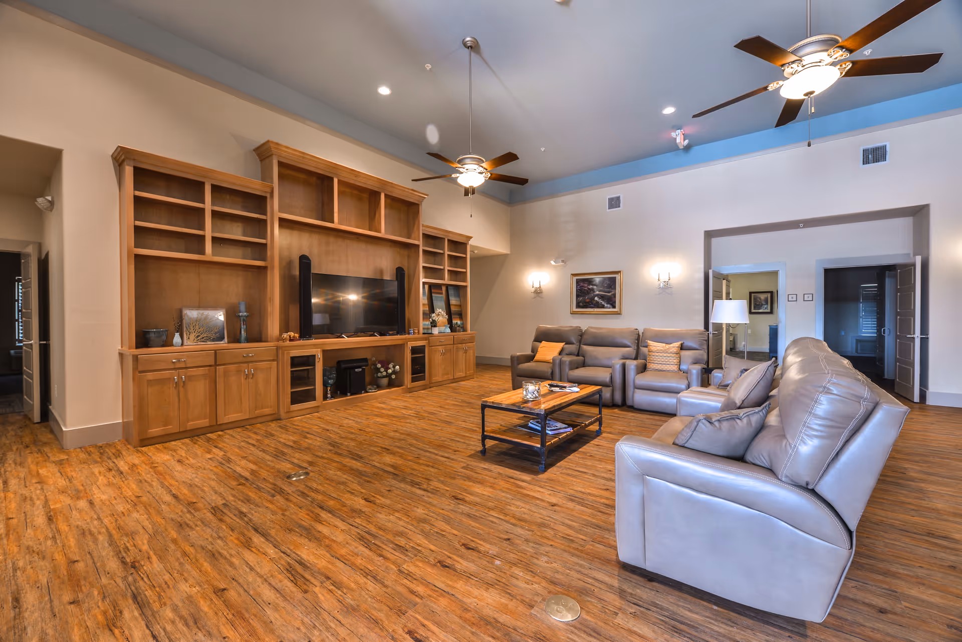Spacious living room featuring a large wooden entertainment center, tan leather seating, and ceiling fans.