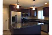 Modern kitchen with dark wood cabinets, a large central island with a dark countertop, stainless steel refrigerator, stove, microwave, and dishwasher. The kitchen is well-lit with two pendant lights hanging over the island and a window above the sink.