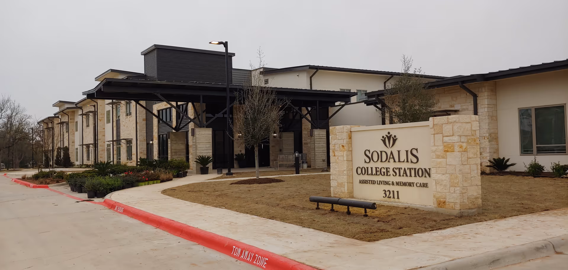 Front exterior of the Sodalis College Station assisted living building with an entrance canopy and a stone sign on the lawn.