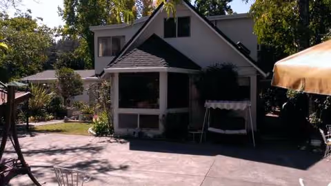 Small house exterior with front porch, screened porch, and outdoor seating on a paved area.