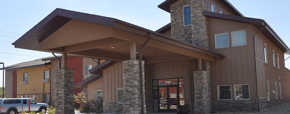 Front exterior and covered entrance of Tradition Assisted Living, featuring stone-clad columns and a two-story brown building.