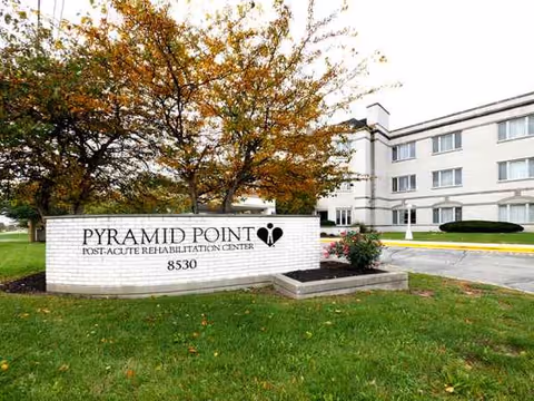 Exterior view of Pyramid Point Post-Acute Rehabilitation Center with sign and white building.
