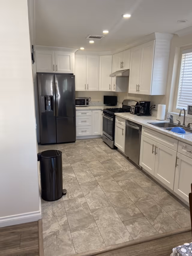 Bright modern kitchen with white cabinets, stainless steel appliances, and gray tiled floor.