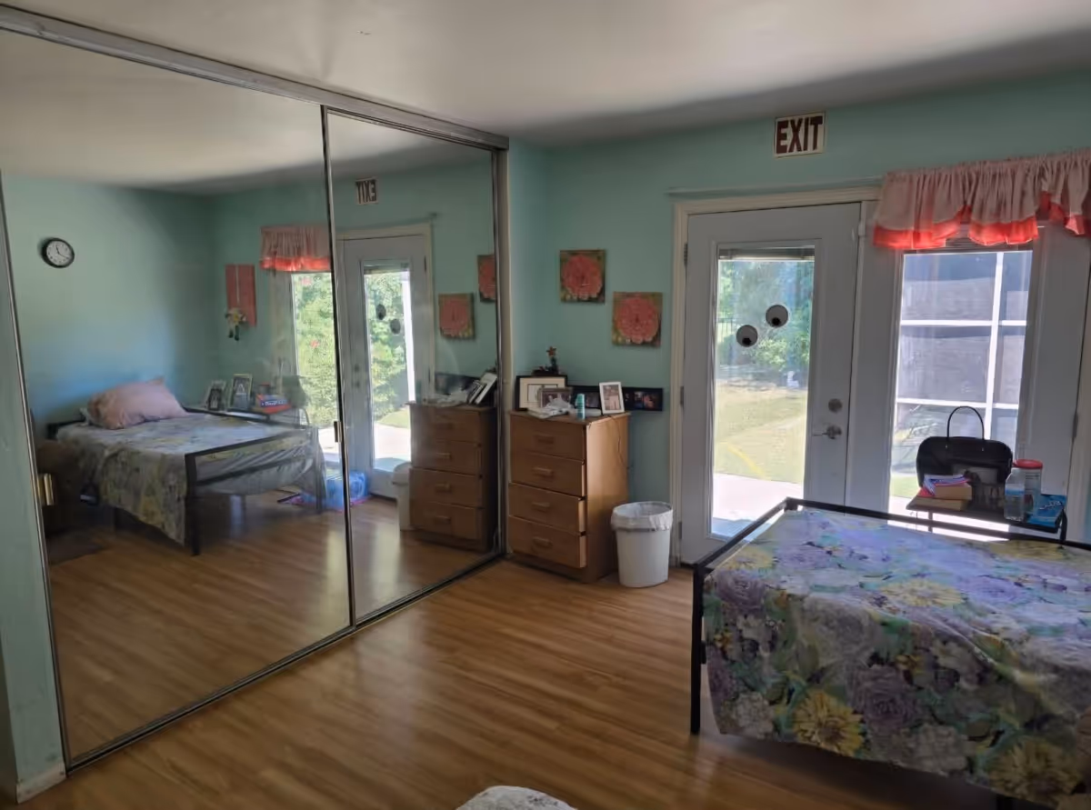 Bright bedroom with two beds, mirrored closet doors, a dresser and an EXIT-marked glass door to the outside.
