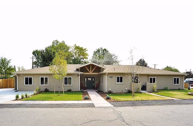 Single-story beige senior living facility with a central entrance, green lawn, and walkway.