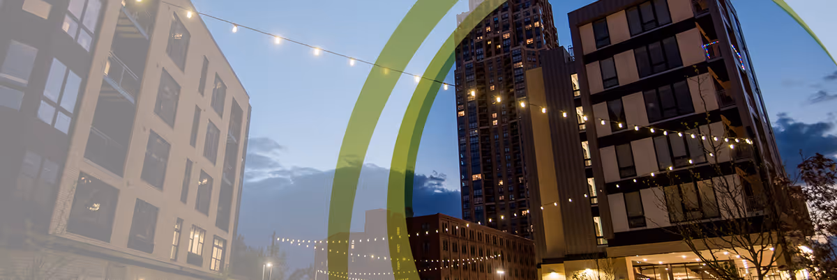 Dusk view of modern multi-story residential buildings with string lights hung across an urban courtyard.