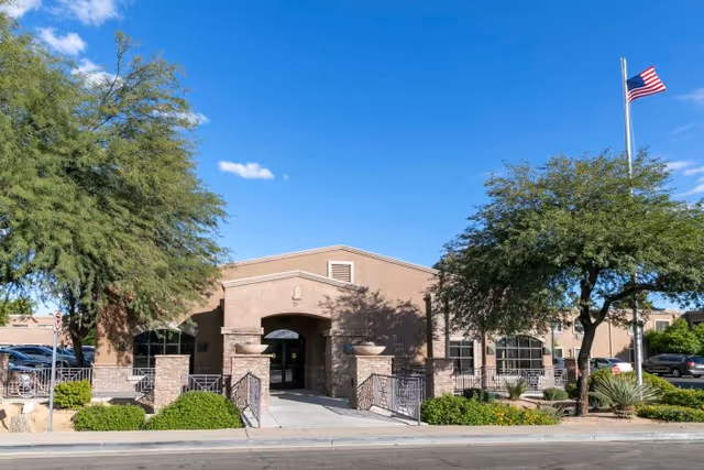 Exterior view of Montecito Post Acute Care And Rehabilitation building with a clear blue sky, trees, shrubs, and an American flag on a flagpole to the right.