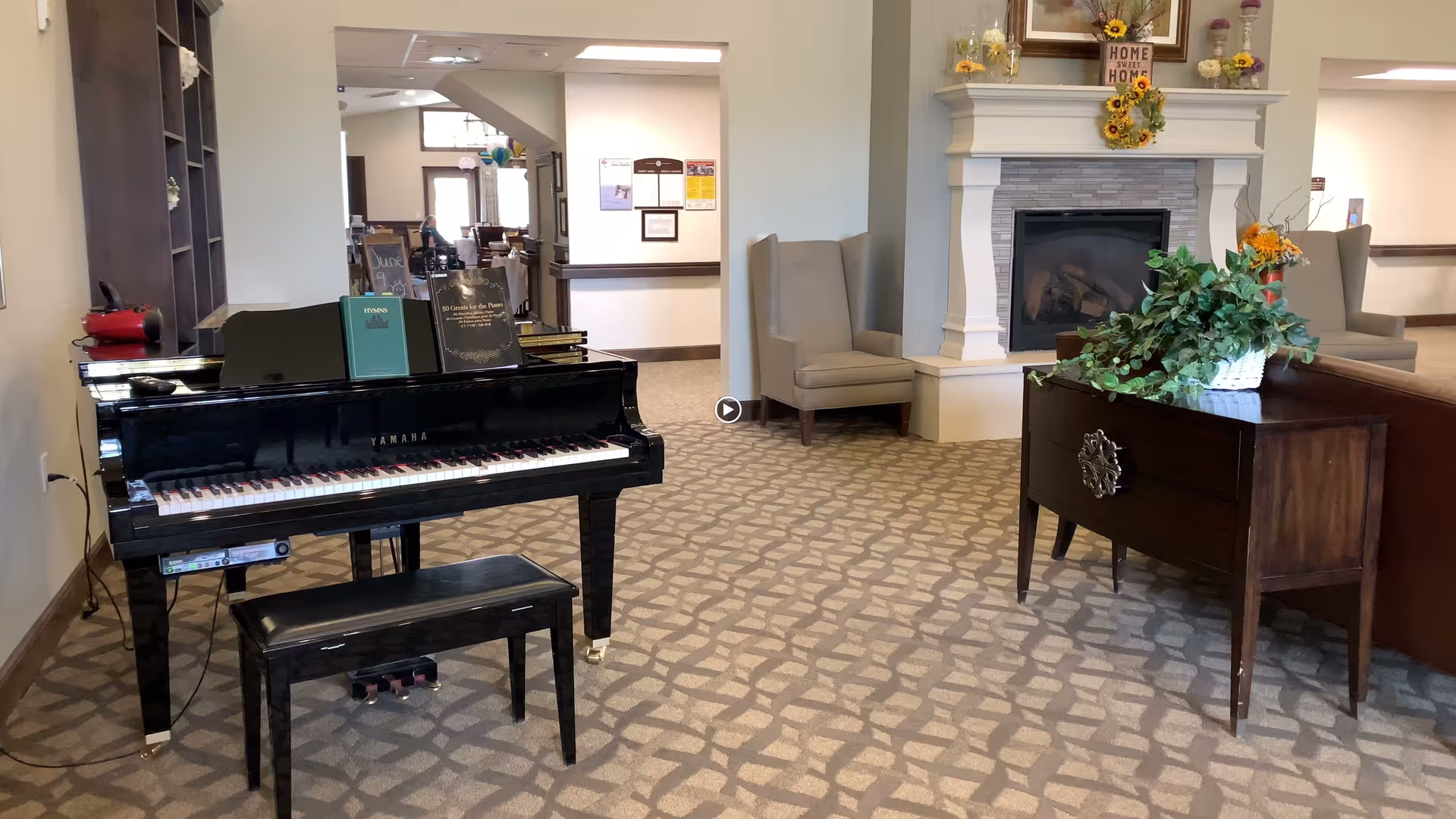 A common living area with a black Yamaha piano, bench, seating, a fireplace, and a side table with a potted plant.