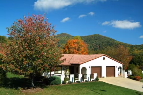 Single-story villa with a red-tiled roof, garages, and fall-colored trees in a mountainous setting.