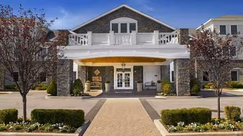 Stone exterior senior living building with white balcony railings and central entrance.