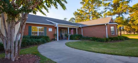 Single-story brick senior living facility with curved front walkway and well-kept lawn.