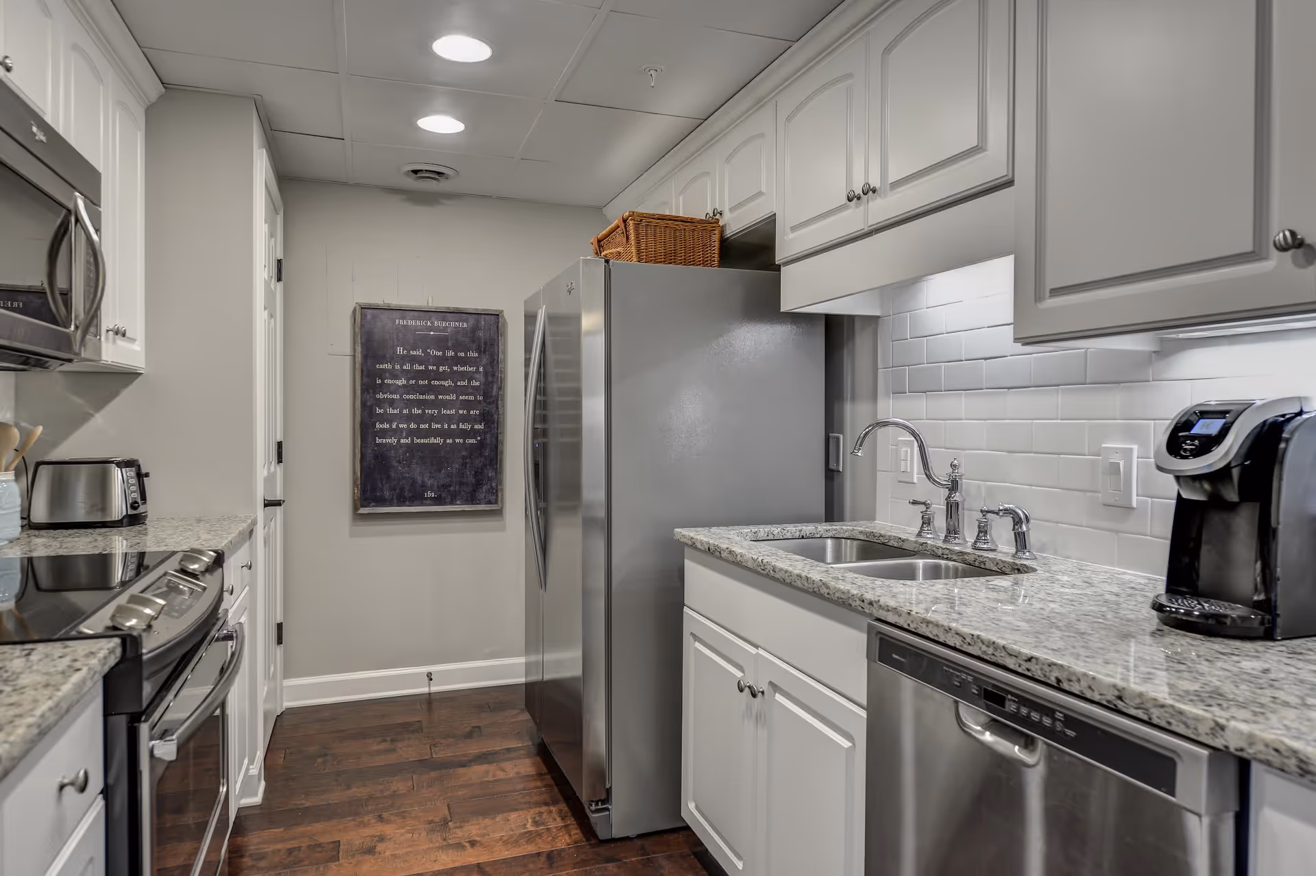 Modern galley kitchen with white cabinets, granite countertops, stainless steel appliances, and a double sink.
