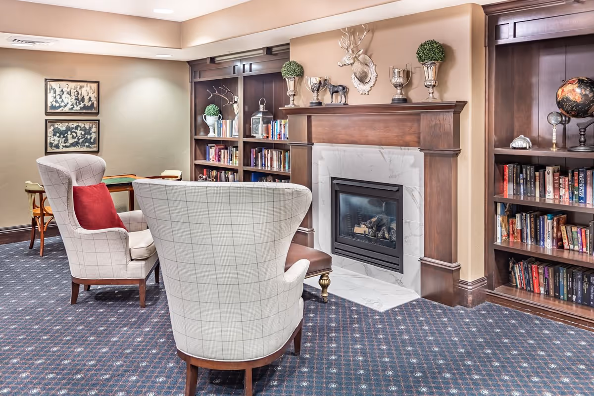 A cozy sitting area with two upholstered armchairs facing a fireplace flanked by wooden bookshelves and decorative items.