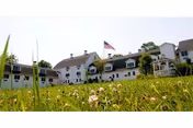 White multi-section senior living building with an American flag in front and a grassy lawn in the foreground.