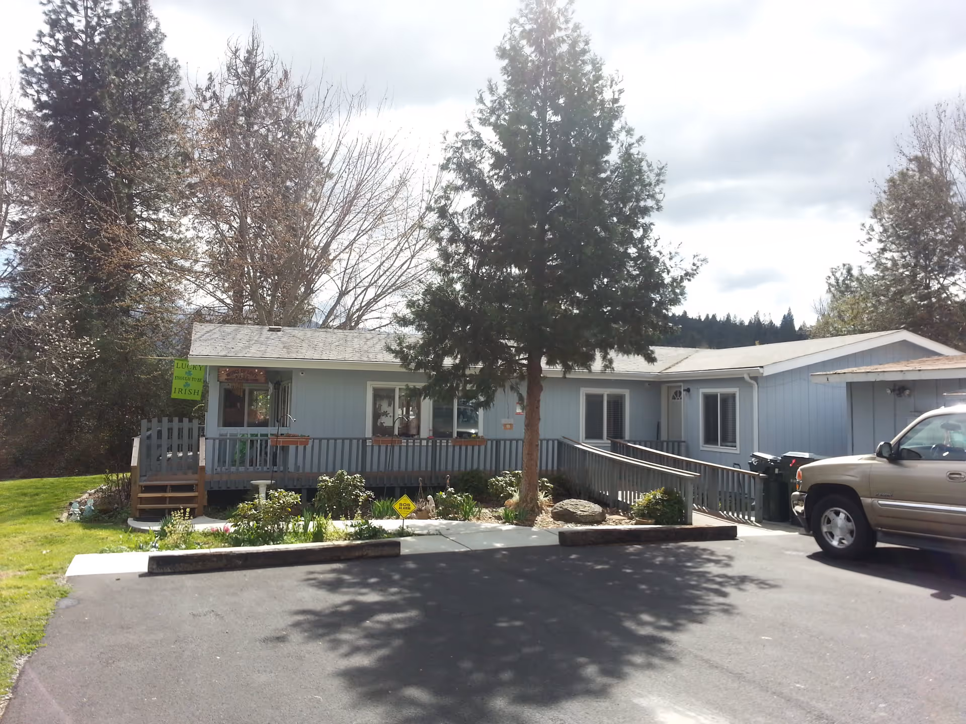 Light-blue single-story building with a front porch and wheelchair ramp, a tree in front, and a parked SUV.