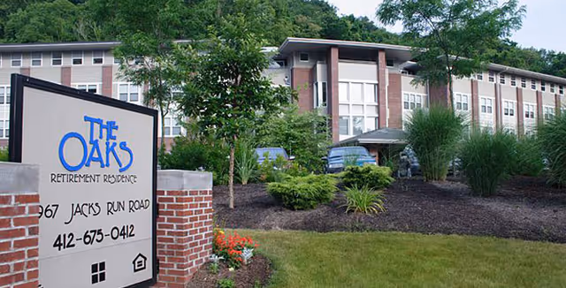 The Oaks Retirement Residence building and landscaped front lawn with an entrance sign in the foreground.