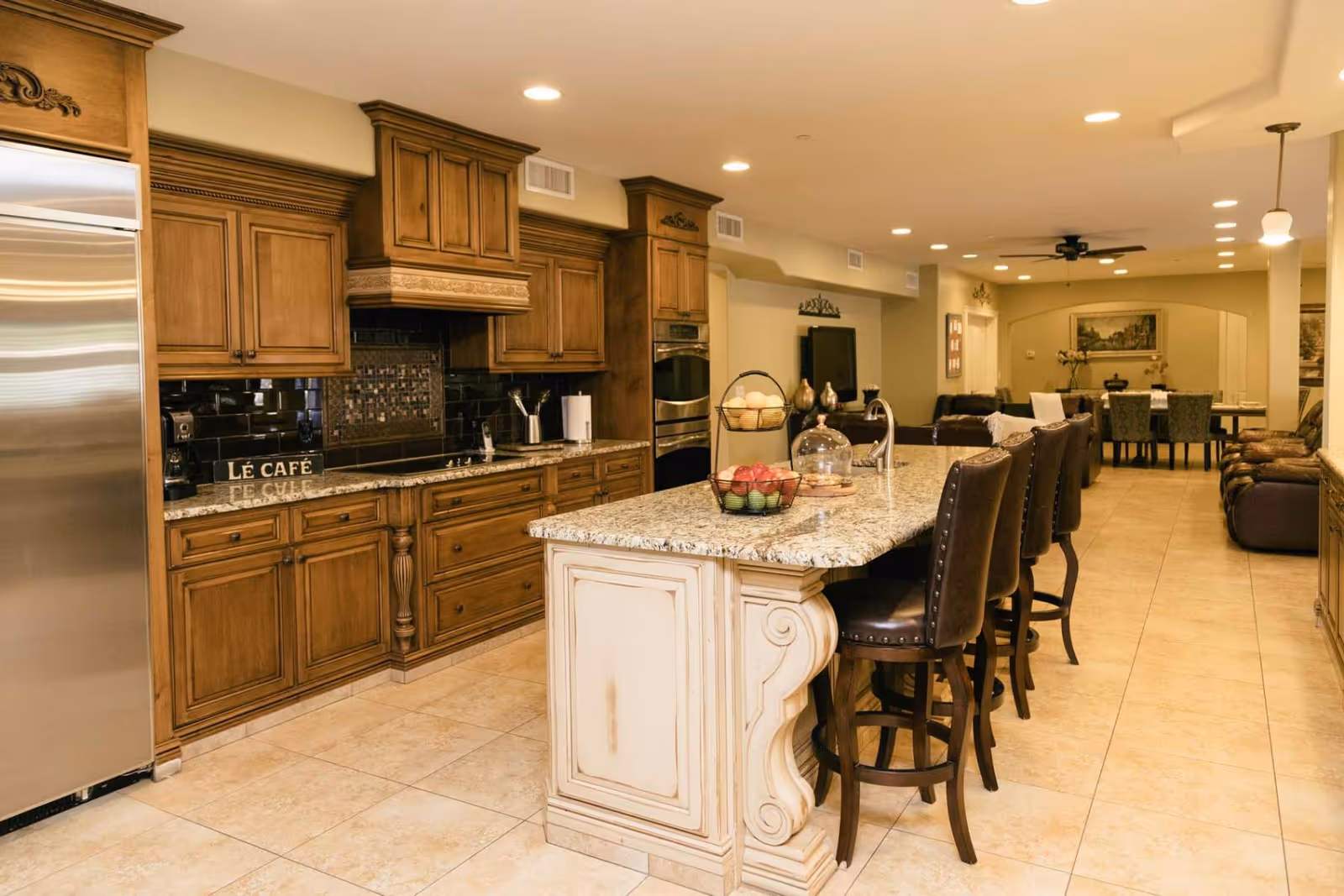 Spacious open-plan kitchen with a large granite island, wooden cabinetry and barstools opening into a living and dining area.
