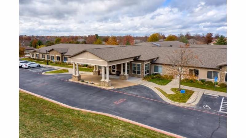Front exterior of a single-story senior living building with a covered entrance, driveway, and parking area.