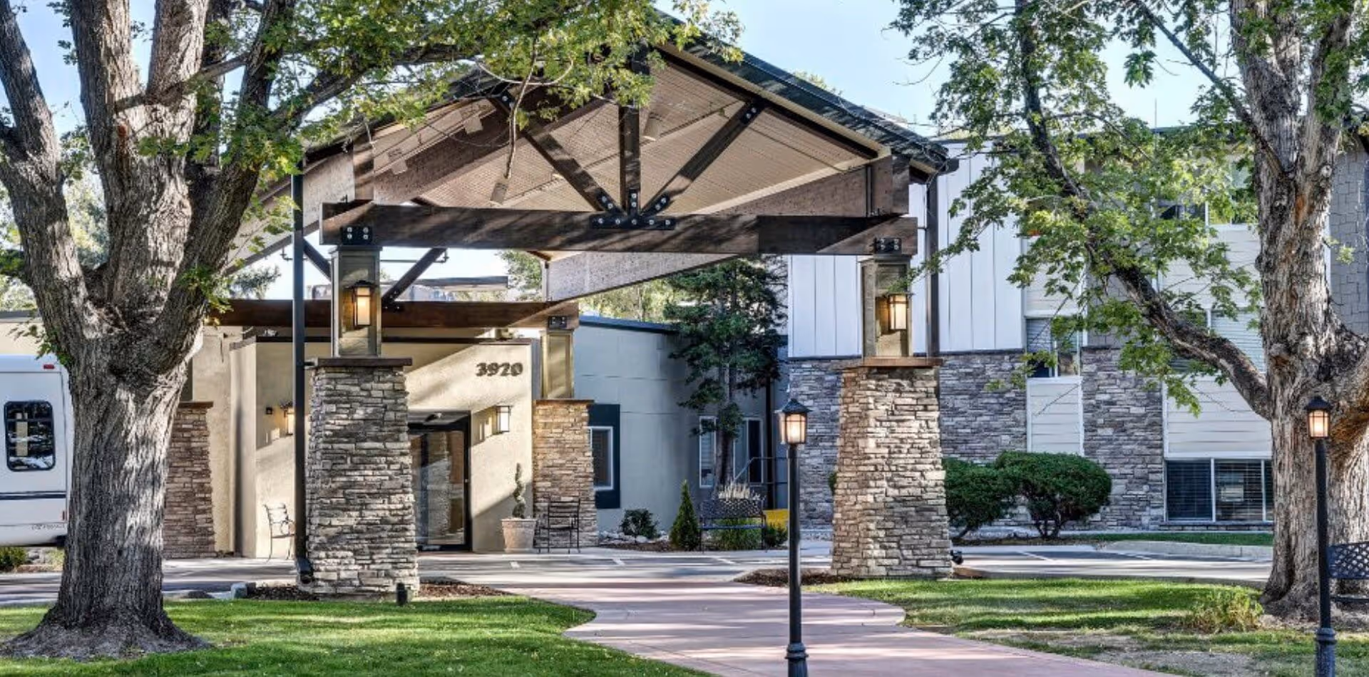 Exterior view of Winslow Court Assisted & Senior Living facility entrance with a covered driveway supported by stone pillars, surrounded by trees and green lawn.