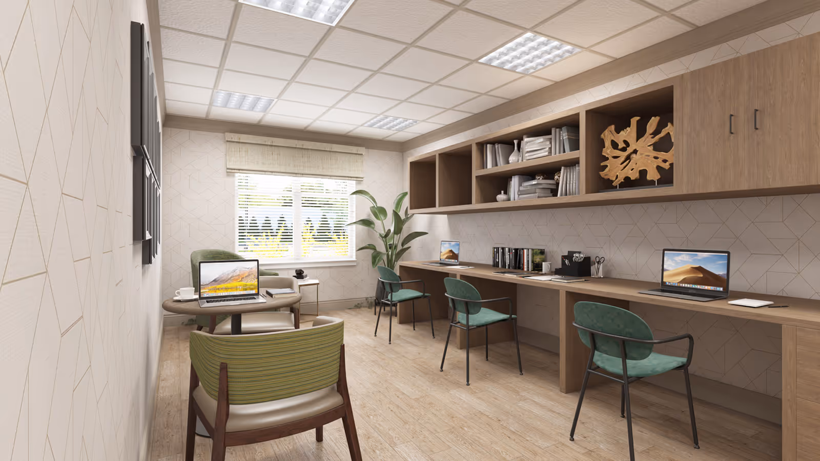 Bright communal workspace with a long wooden desk, green chairs, laptops, bookshelves and a small seating area by a window.