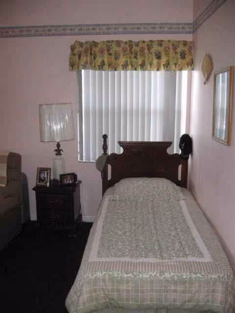 Single bed with wooden headboard in a pink-themed bedroom with nightstand and window blinds.