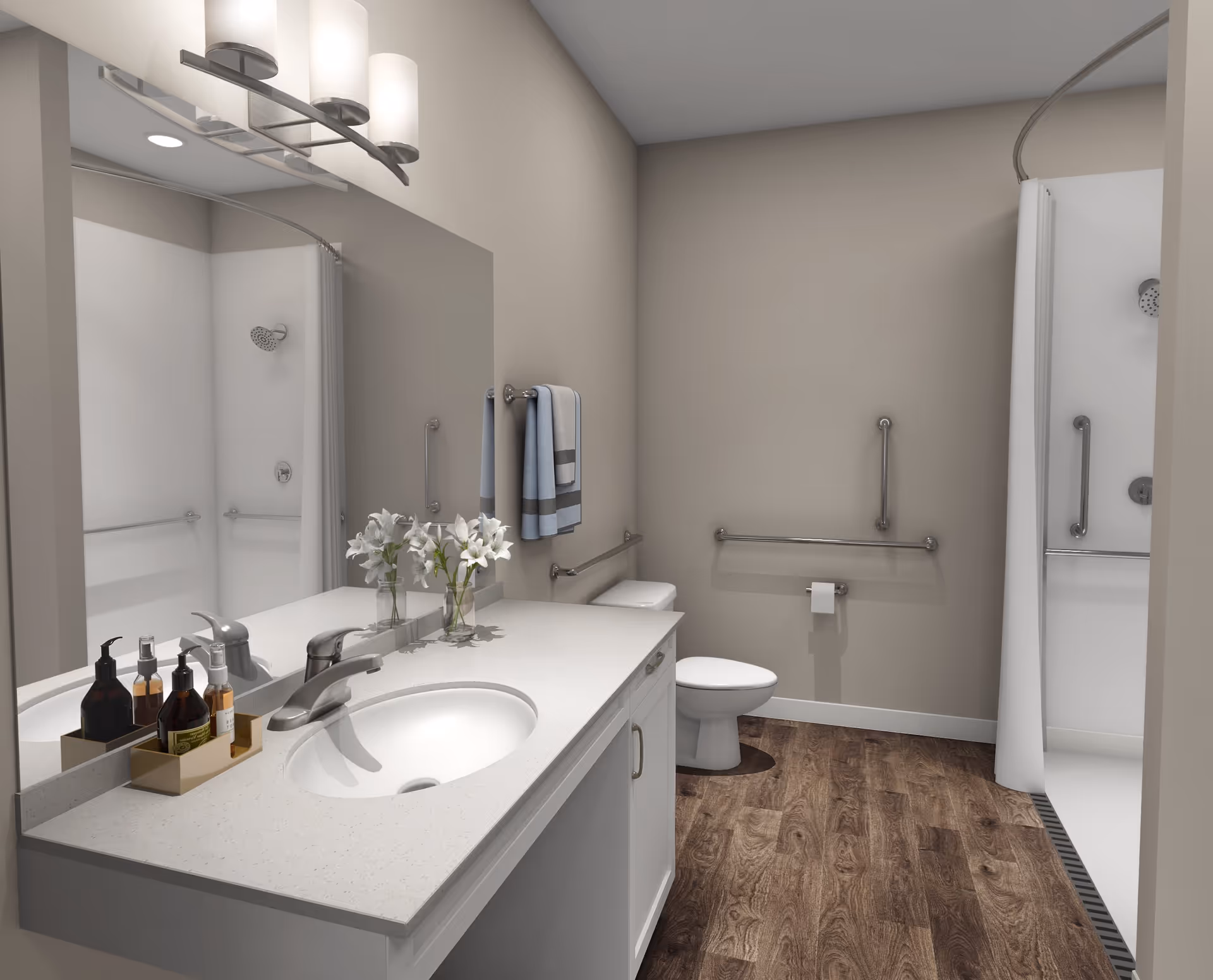 A modern bathroom with a white countertop sink, a large mirror, and a vase with white flowers. There are handrails on the walls near the toilet and inside the shower area, which has a curved shower curtain rod. The floor has a wood-like finish, and the walls are painted beige.