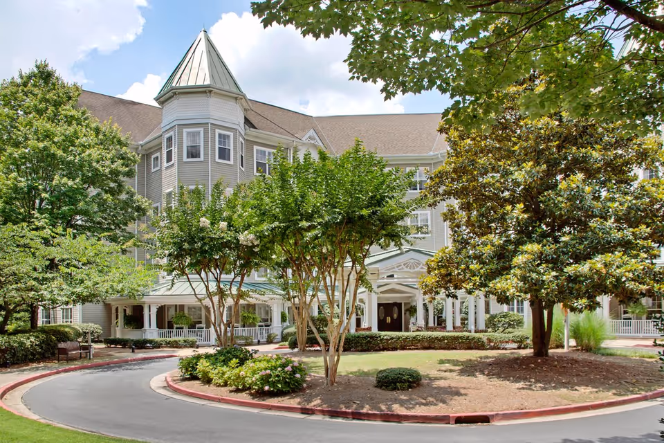 Front exterior of a multi-story senior living building with a circular driveway, trees, and a covered entrance.