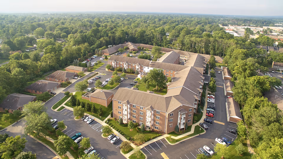 Aerial view of a multi-building brick senior living complex with parking lots and surrounding trees.