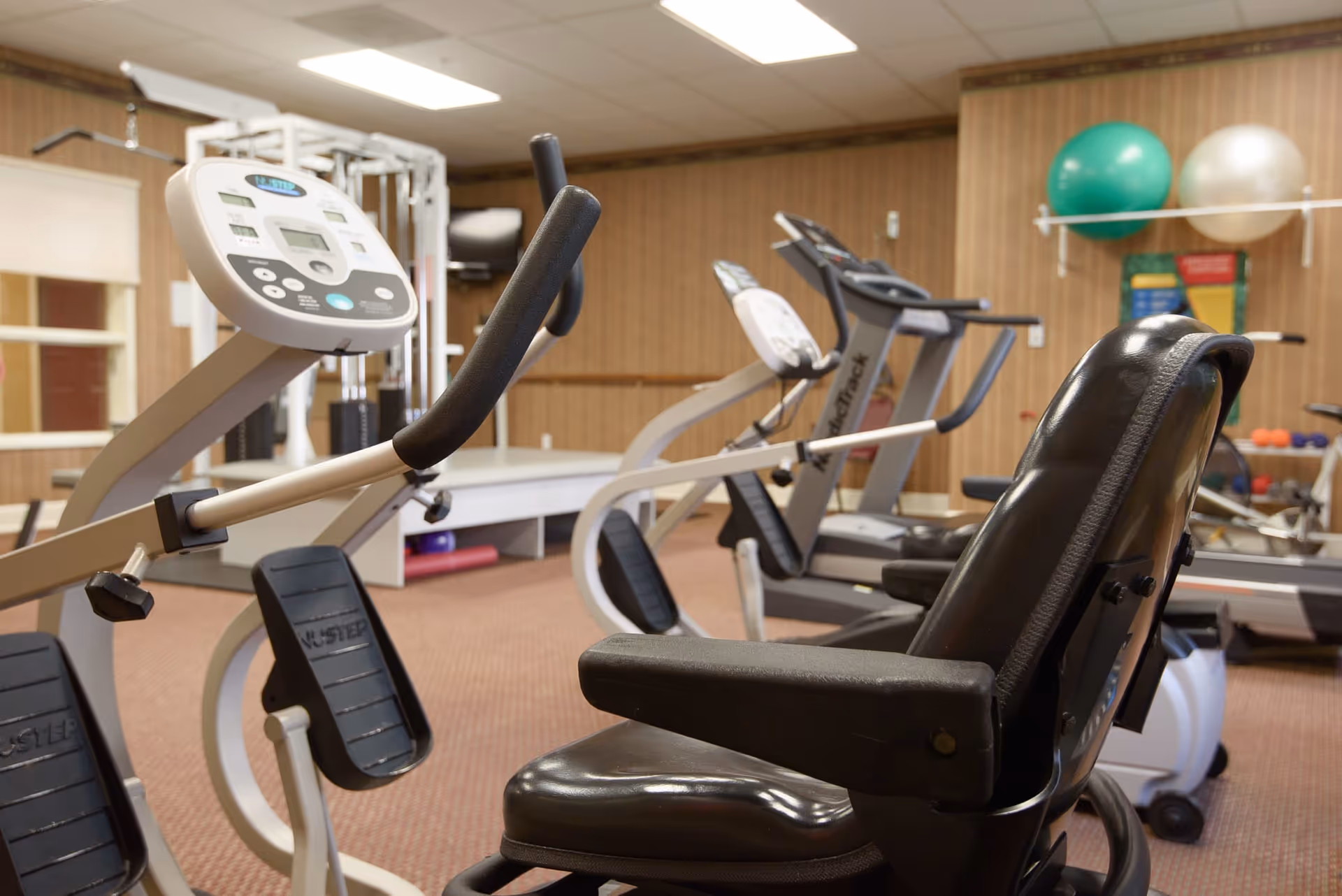 An indoor fitness room with recumbent exercise bikes, treadmills, and stability balls.