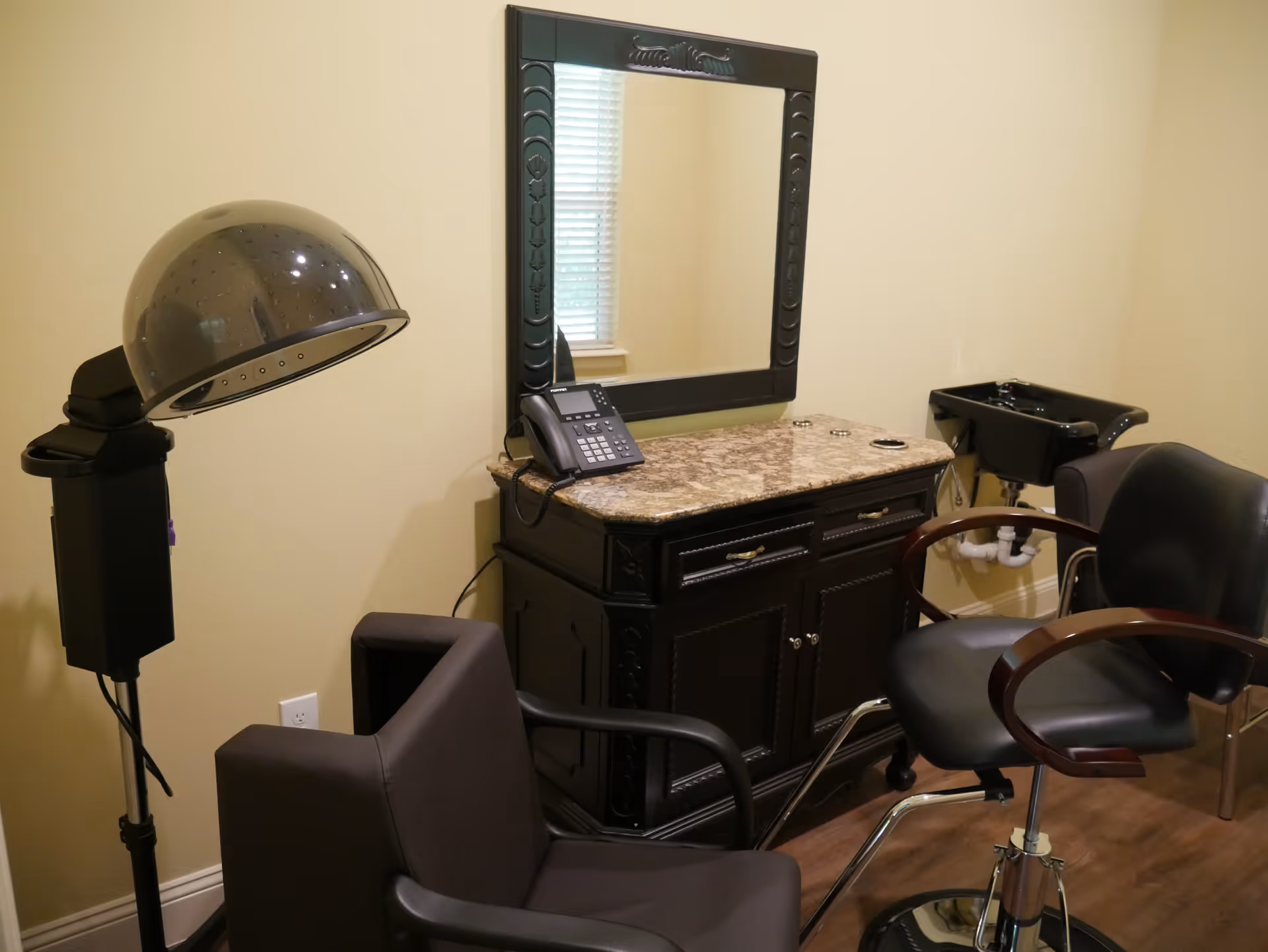 Salon-style room with styling chairs, a hooded hair dryer, mirror, countertop cabinet, and a wash basin.