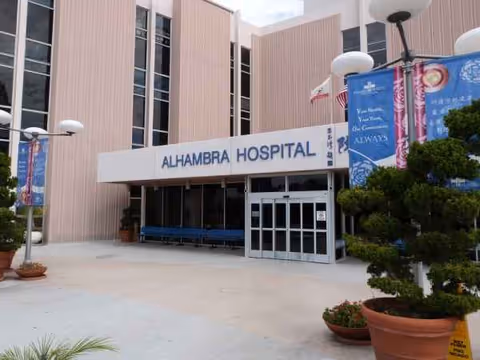 Exterior view of Alhambra Hospital Medical Center entrance with benches and potted plants.
