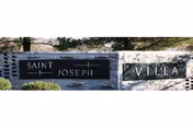 Stone entrance sign on a low wall that reads 'Saint Joseph Villa' with shrubs in front.