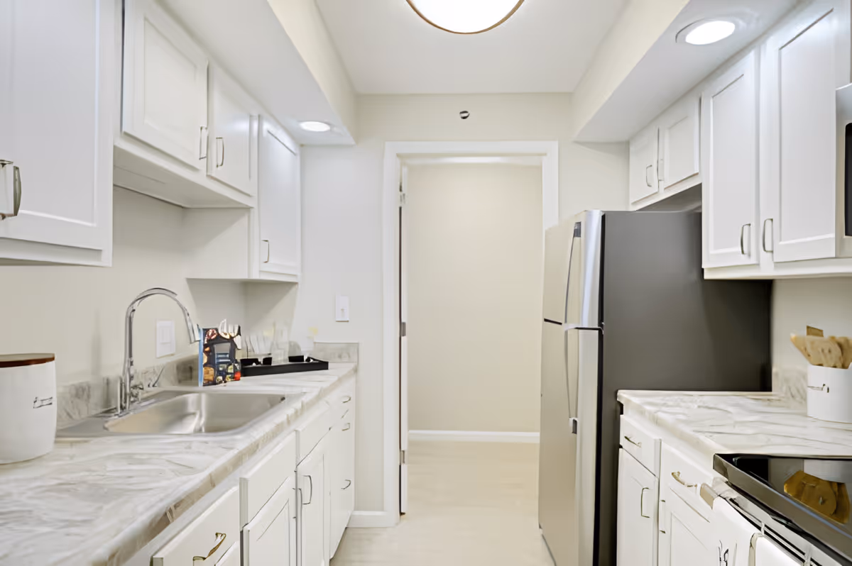 Bright modern kitchen with white cabinets, marble countertops, a stainless steel sink and refrigerator.