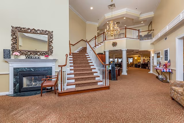 Spacious interior lobby with a central carpeted staircase, chandelier, fireplace, and seating areas.