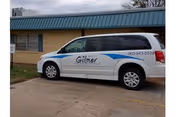 White van labeled 'Gilmer' parked in front of a single-story building with a green metal awning.