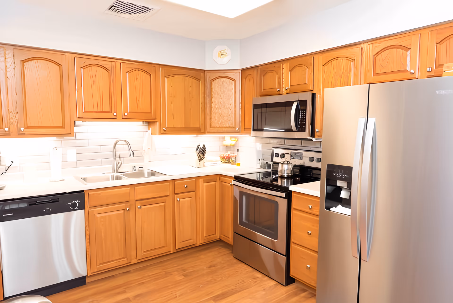 Bright kitchen with wooden cabinets, stainless steel refrigerator, stove, microwave, dishwasher and a double sink.
