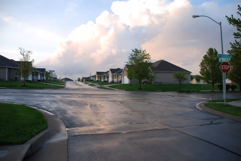 Wet residential street intersection with single-story houses, trees, a stop sign and a cloudy sky.