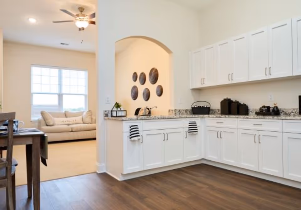 Bright open kitchen with white cabinets and granite countertops opening to a living area with a beige sofa.