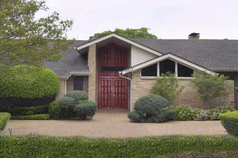 Front view of brick senior living facility with a red door and landscaped shrubs.